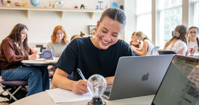 A female student takes notes in front of her laptop while working in a small group